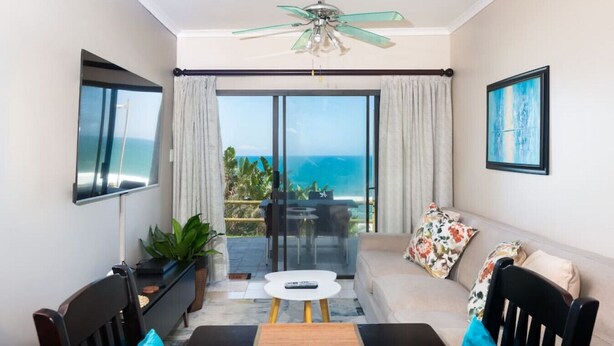A modern living room with a glass door leading to a balcony with a view of the ocean.