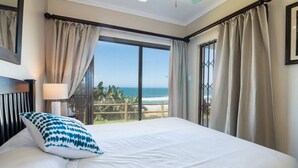 A bedroom with a large bed, a view of the ocean, and a balcony with curtains.