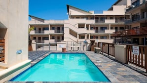 A swimming pool with a stone deck, surrounded by multi-story buildings with balconies.