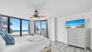 A bedroom with a bed, a ceiling fan, a view of the beach, and a TV on a dresser. - Edgewater Tower 3-104 (Panama City Beach)