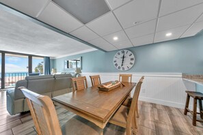 A dining area with a wooden table, chairs, and a large wall clock.
