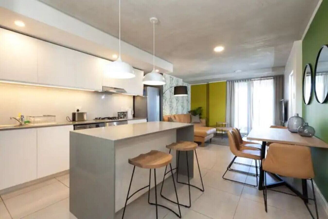 A modern kitchen with a central island, bar stools, and a dining area with a table and chairs.