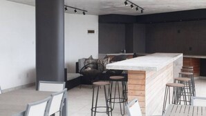 Un espace bar moderne doté d’un îlot central, de tabourets de bar et d’un coin salon avec un canapé et des fauteuils.