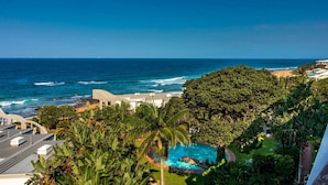 Vista costera con piscina rodeada de exuberante vegetación y una playa al fondo.