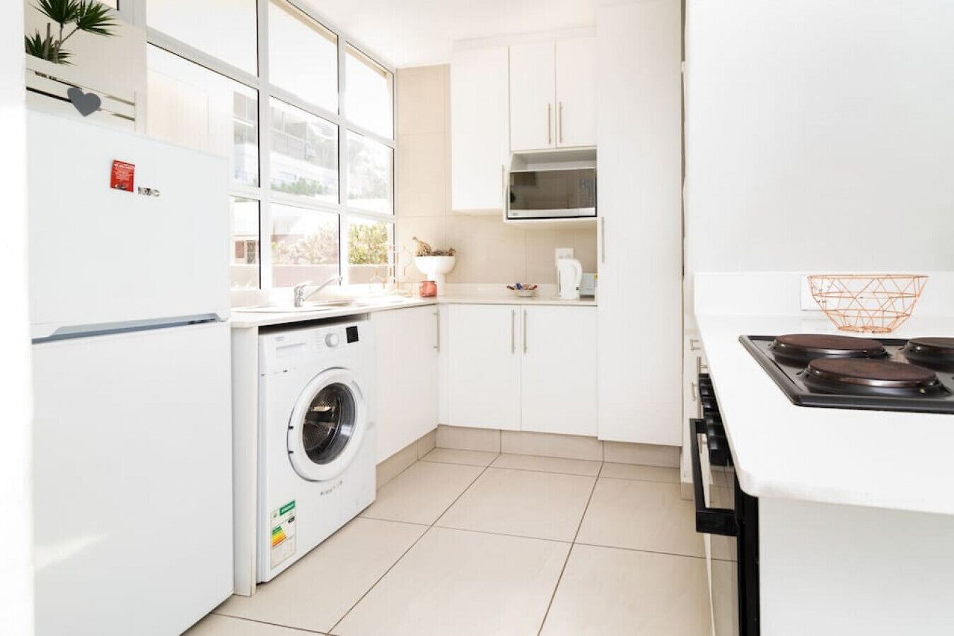 A modern kitchen with a built-in washer, white cabinets, a microwave, and a stove.