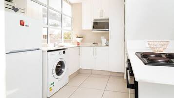 A modern kitchen with a built-in washer, white cabinets, a microwave, and a stove.