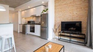 A modern kitchen with stainless steel appliances, a dining area with a wooden table, and a living space with a TV and seating. - Coral Point Executive Studio Apartment E316 (Sibaya Precinct)