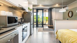 A modern kitchen with a microwave, stove, and oven. There is a dining area with a table and chairs, and a bed with a yellow striped blanket. - Coral Point Executive Studio Apartment E316 (Sibaya Precinct)