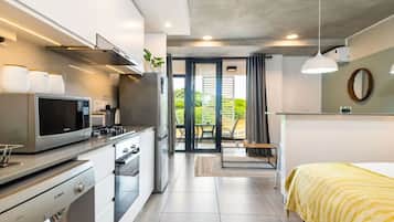 Una cocina moderna con microondas, estufa y horno. Hay un comedor con mesa y sillas, y una cama con una colcha amarilla a rayas.