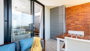 Ein Balkon mit Glastür, einem Holztisch und einer Couch mit Kissen.