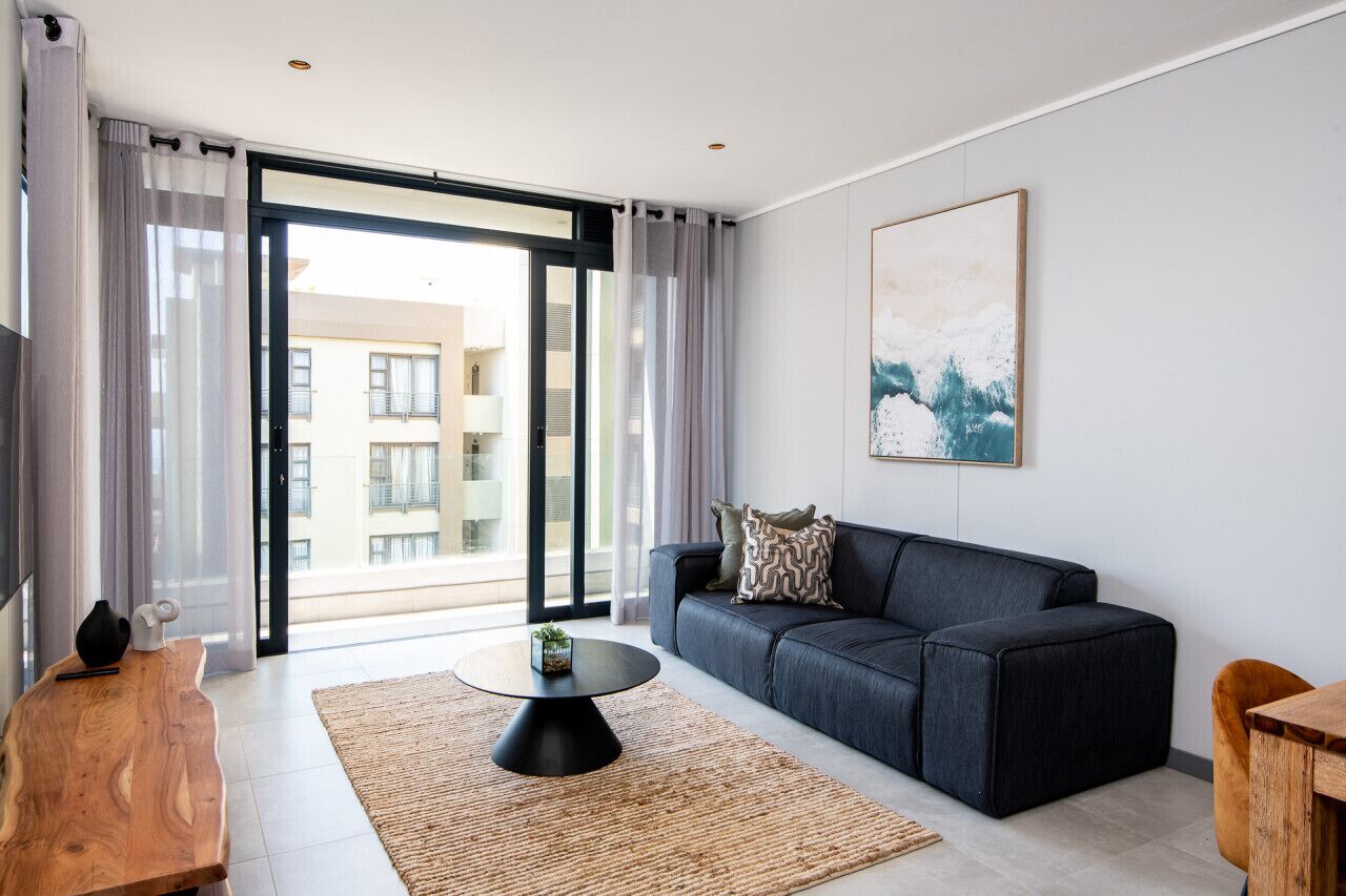 A modern living room with a dark grey sofa, a round coffee table, and a wooden side table.