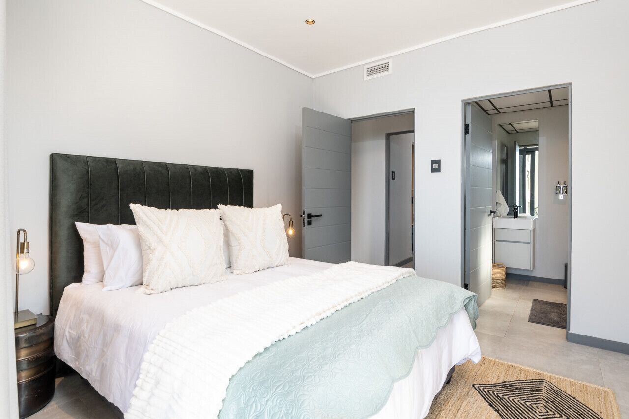 A bedroom with a large bed, bedside lamps, a mirror, and a door leading to another room.