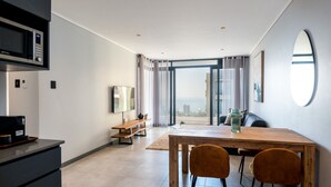 Un salon moderne avec une table à manger en bois, deux chaises, un canapé et une grande fenêtre donnant sur la ville.