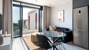 A modern living room with a glass dining table, dark sofas, and a large refrigerator. - Luxury Bellagio 303 (uMhlanga Ridge, KwaZulu-Natal)