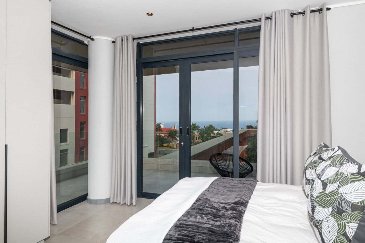 Ein Schlafzimmer mit Bett, Blick auf die Stadt und einem Balkon mit Vorhängen.