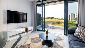 A modern living room with a flat-screen TV, a glass coffee table, and a sofa with a patterned cushion. - Luxury Bellagio 003 (uMhlanga Ridge, KwaZulu-Natal)