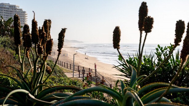 A beach with a wooden walkway and a building in the background. - Luxury Bellagio 003 (uMhlanga Ridge, KwaZulu-Natal)