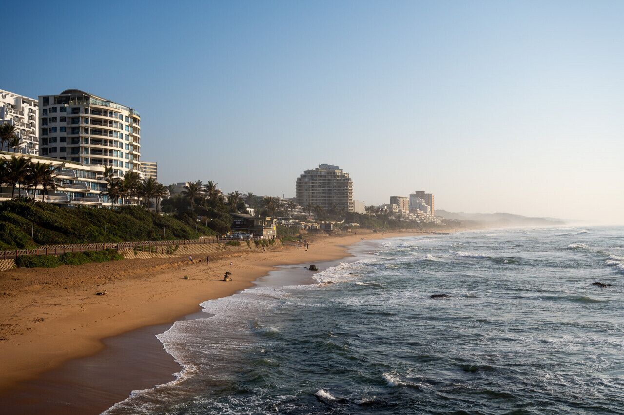 A beach with a sandy shore, a few people, and buildings in the background.