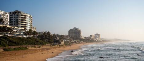 A beach with a sandy shore, a few people, and buildings in the background.