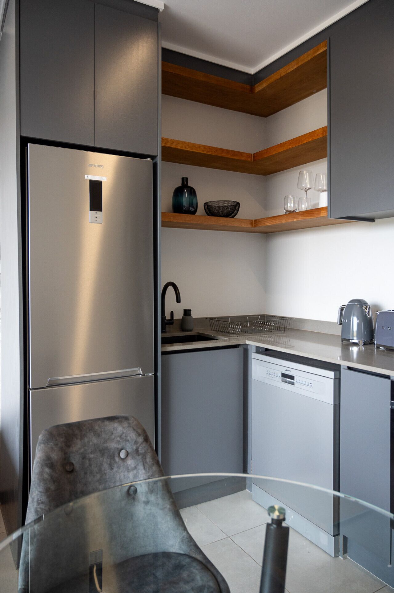 Une cuisine moderne avec des meubles de couleur grise, un réfrigérateur en acier inoxydable, un lave-vaisselle encastré et des étagères en bois au-dessus du plan de travail.