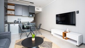 A modern kitchen with grey cabinets, a built-in microwave, and a coffee machine. There is a dining area with a round table and chairs, and a TV mounted on the wall. - Luxury Bellagio 003 (uMhlanga Ridge, KwaZulu-Natal)