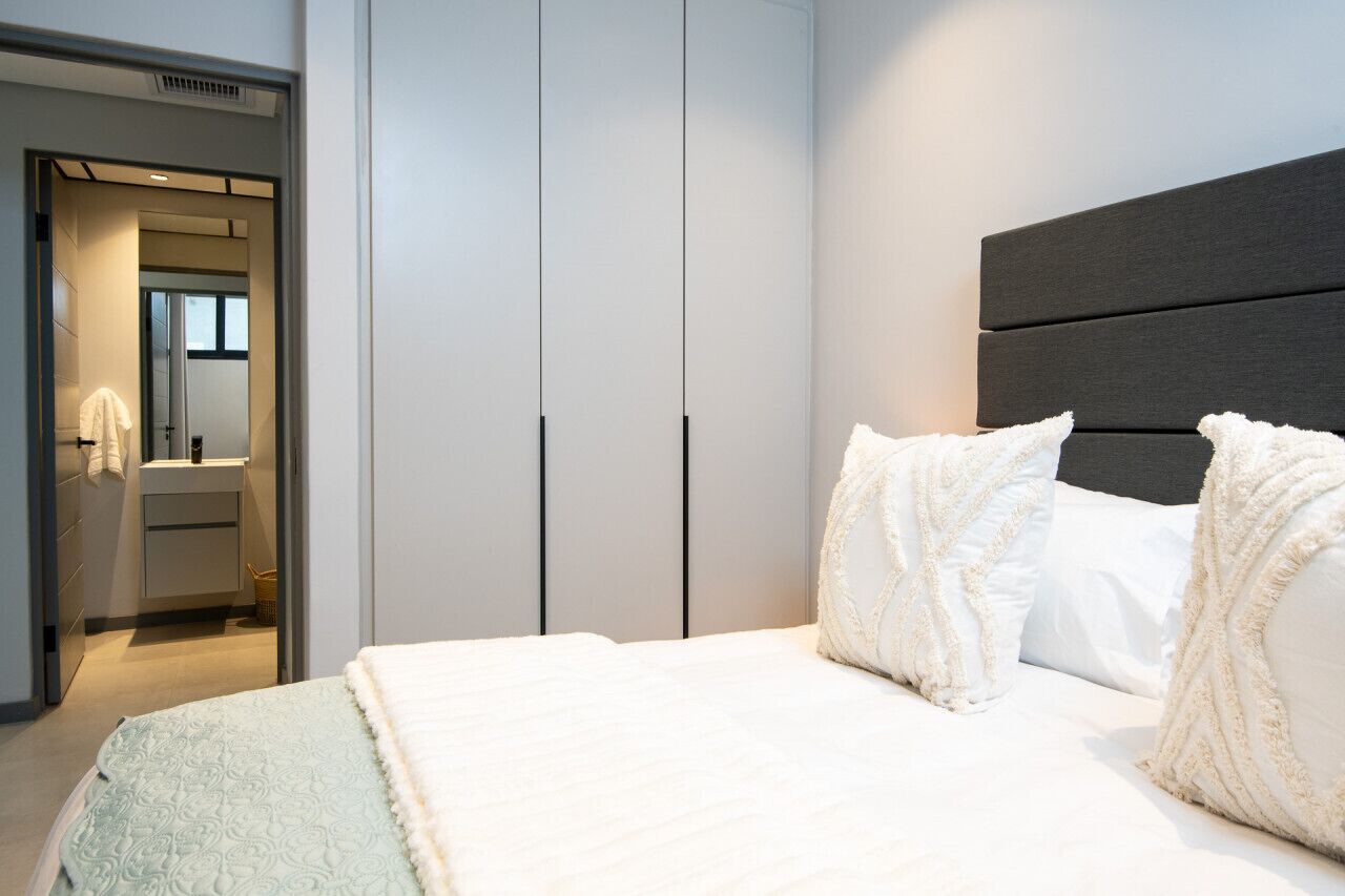 Ein modernes Schlafzimmer mit einem großen Bett, einem Kleiderschrank und einem durch eine offene Tür einsehbarer Badezimmer.