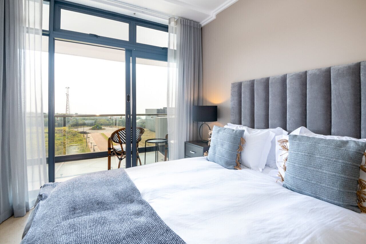 Een hotelkamer met een groot bed, uitzicht door een schuifdeur, een stoel en een bijzettafeltje.