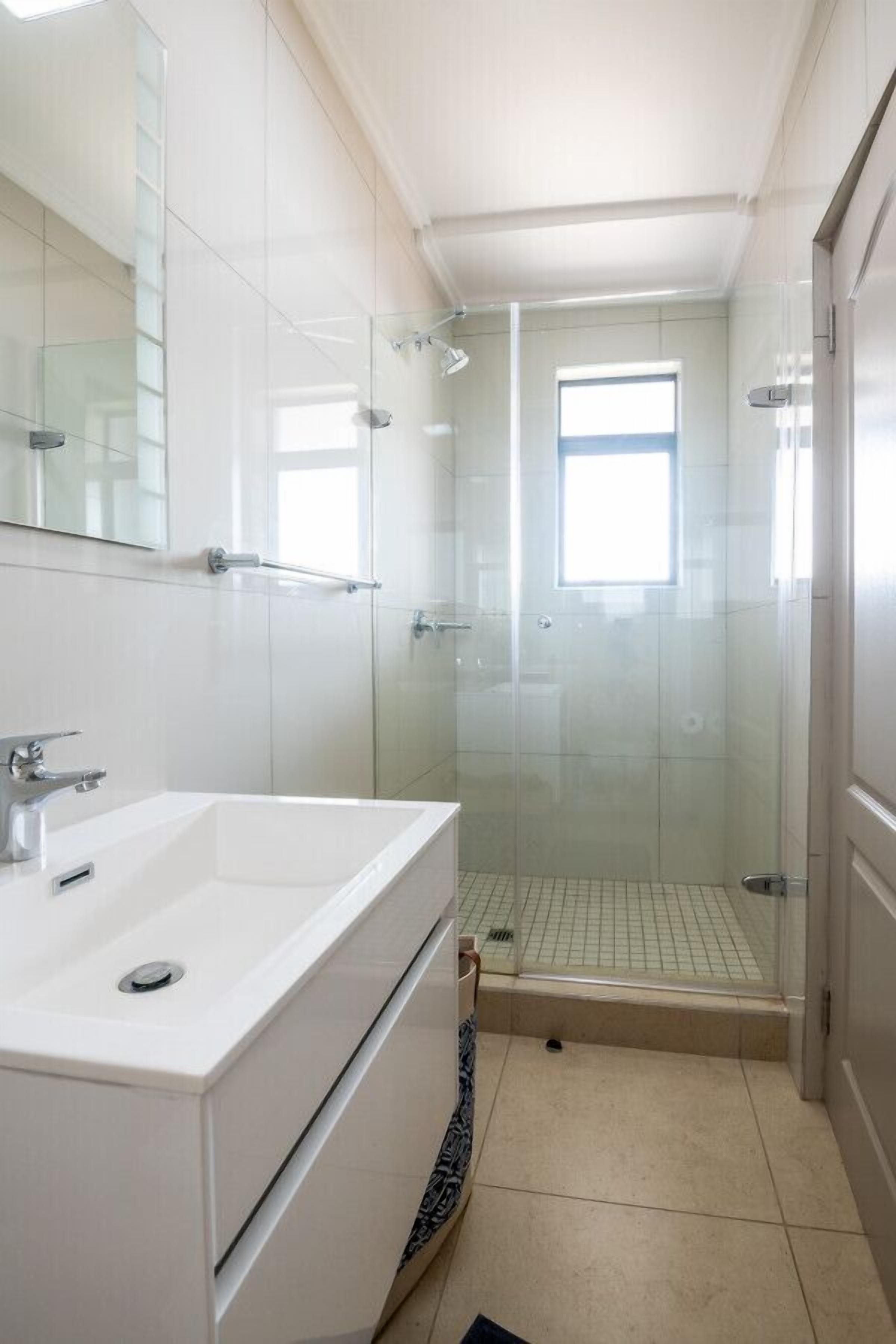 Un baño moderno con ducha envuelta en vidrio, un lavabo blanco y un espejo grande.