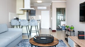 Ein modernes Wohnzimmer mit grauem Sofa, einem runden Couchtisch und einer Küchenzeile mit weißem Schrank und grauem Sessel.