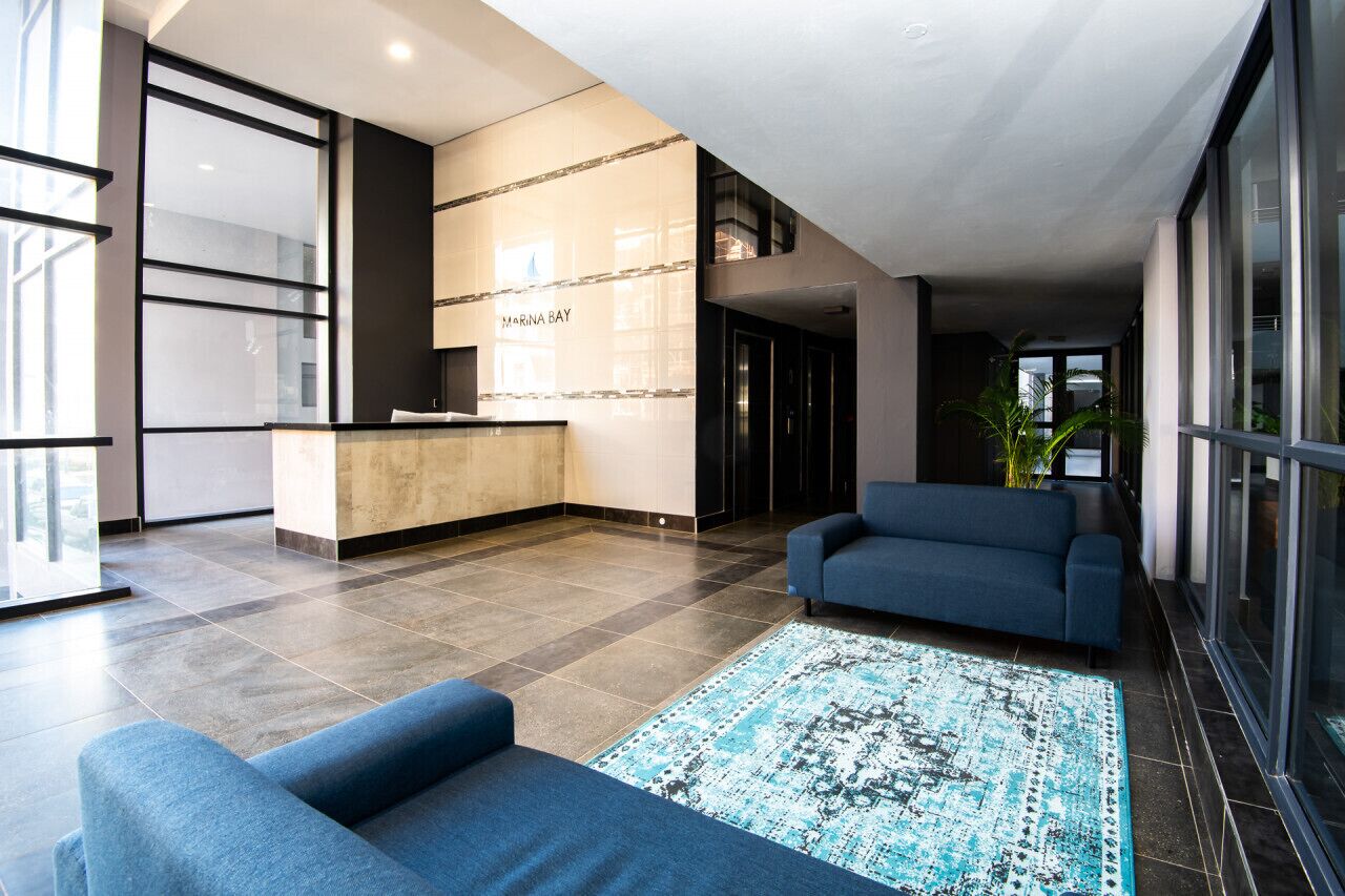 Een moderne lobby met een receptiebalie, een blauwe bank en een getextureerd vloerkleed.