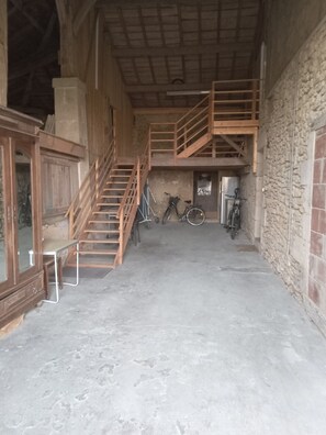 A spacious interior with a wooden staircase leading to an upper level, a stone wall, and bicycles parked against the wall.
