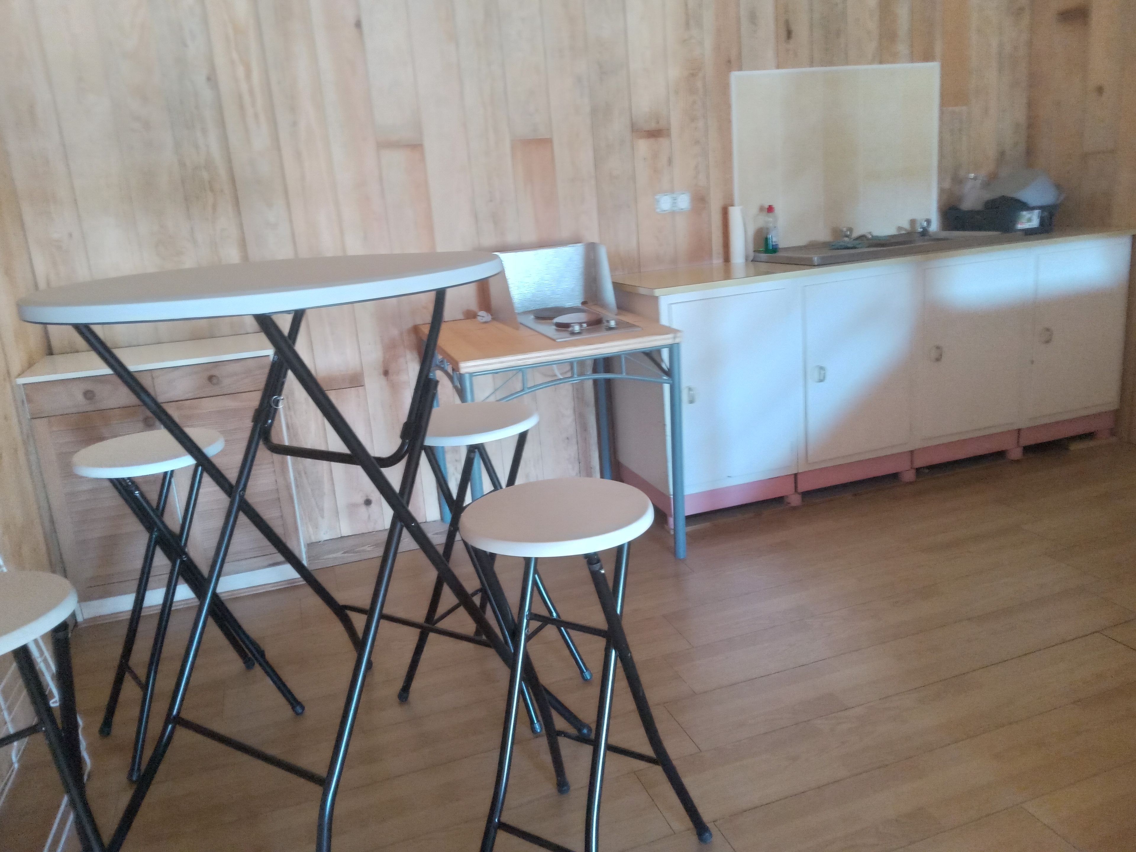 A kitchen with a wooden wall, a white countertop, and a sink. There are four stools and a table with a metal frame.