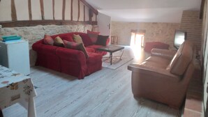 Un salón acogedor con un sofá rojo, un sillón marrón y una mesita. Un televisor está montado en la pared.