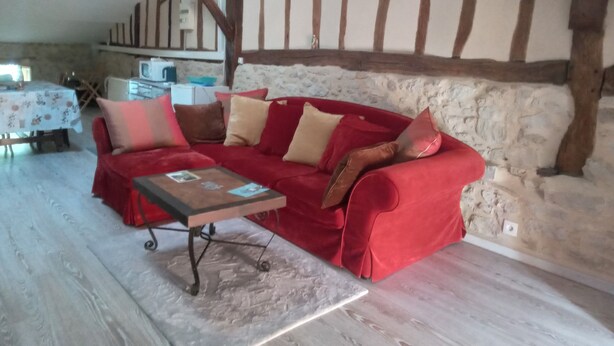 Un sofá rojo con varios cojines en una habitación rústica con vigas de madera a la vista y pared de piedra.