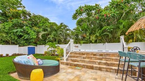 A backyard with a hot tub, a wicker chair, and a yellow vase. - SwimSpa Oasis Backyard Beach 1.5 mi Monthly Stays (Naples)