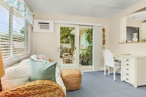 Une chambre à coucher avec un lit, un bureau et une chaise. Il y a une fenêtre avec des stores et une porte qui donne sur un balcon.