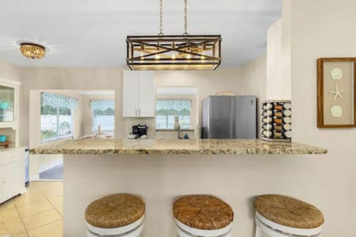 A kitchen with a central island, bar stools, a hanging light fixture, and a refrigerator.
