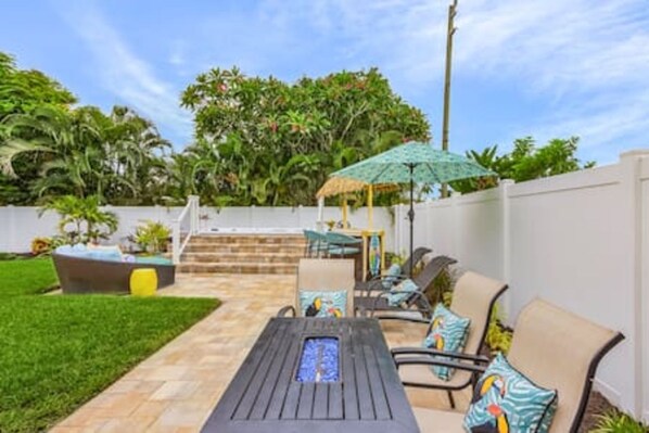 A patio with a table and chairs, a small umbrella, and a staircase leading to a deck.