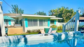 A swimming pool with a hot tub, a covered area with chairs, and a building with a white facade and blue shutters. - SwimSpa Oasis Backyard Beach 1.5 mi Monthly Stays (Naples)