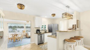 A modern kitchen with white cabinets, a stainless steel refrigerator, and a dining area with a table and chairs. - SwimSpa Oasis Backyard Beach 1.5 mi Monthly Stays (Naples)