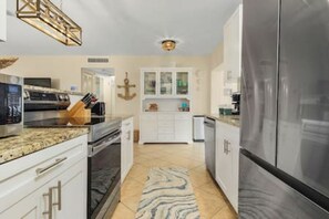 A modern kitchen with stainless steel appliances, white cabinetry, and a marble countertop.