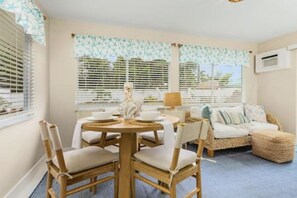 Una habitación con una mesa de comedor preparada para cuatro personas, un sofá y una ventana con persianas.