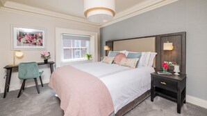 Un dormitorio con cama, mesita de noche, silla, escritorio y ventana.
