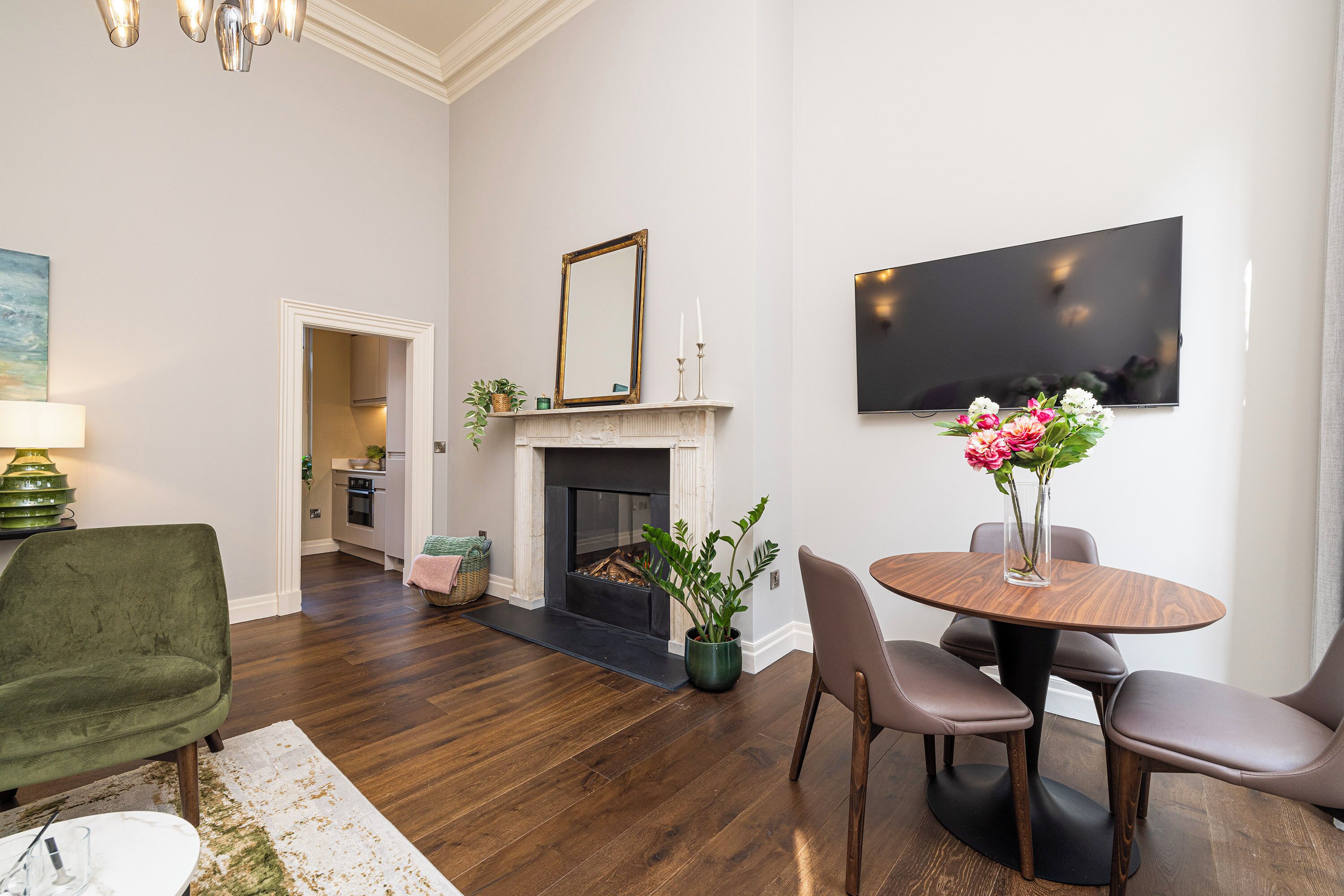 A living room with a fireplace, a dining table with chairs, a green armchair, and a TV mounted on the wall.