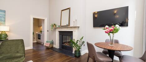 A living room with a fireplace, a dining table with chairs, a green armchair, and a TV mounted on the wall.