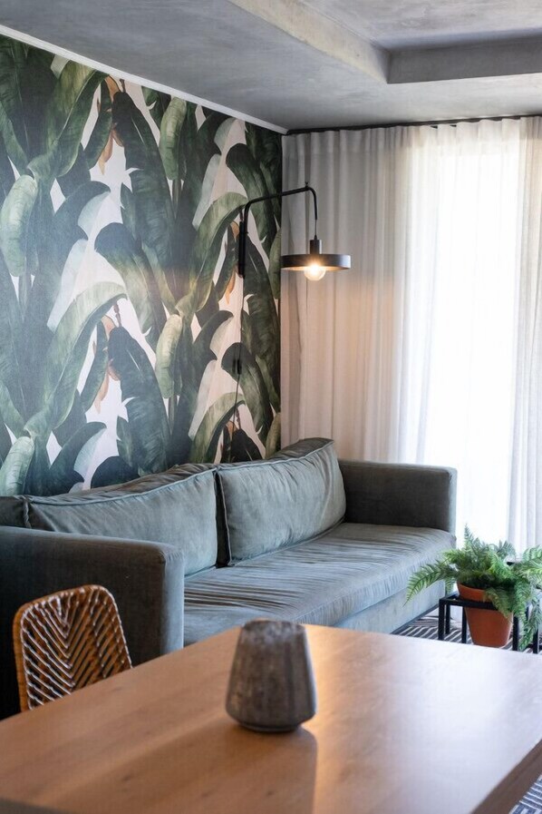 A modern living room with a grey sofa, a wooden coffee table, and a wall with a tropical leaf pattern.