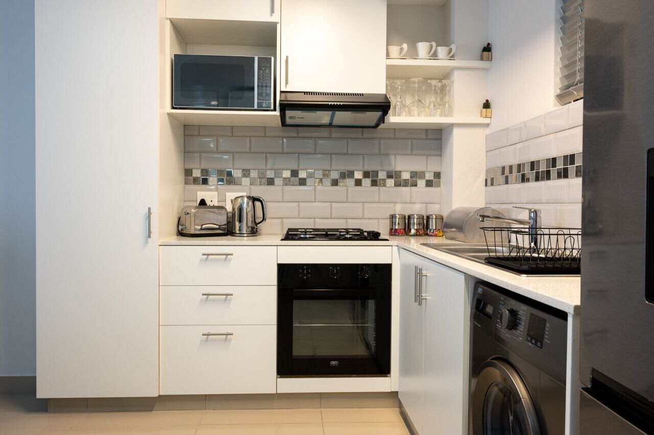 Una cocina compacta con armarios blancos, microondas integrado, estufa, horno y lavavajillas.