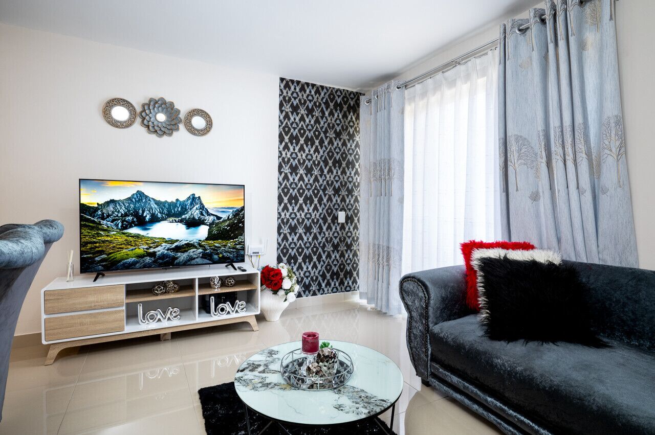 A modern living room with a flat-screen TV, a black sofa, a white coffee table, and a patterned wall.