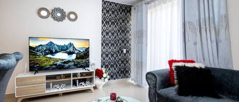 A modern living room with a flat-screen TV, a black sofa, a white coffee table, and a patterned wall.
