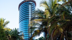 Un grand bâtiment cylindrique surmonté d’une coupole incurvée, entouré de palmiers.